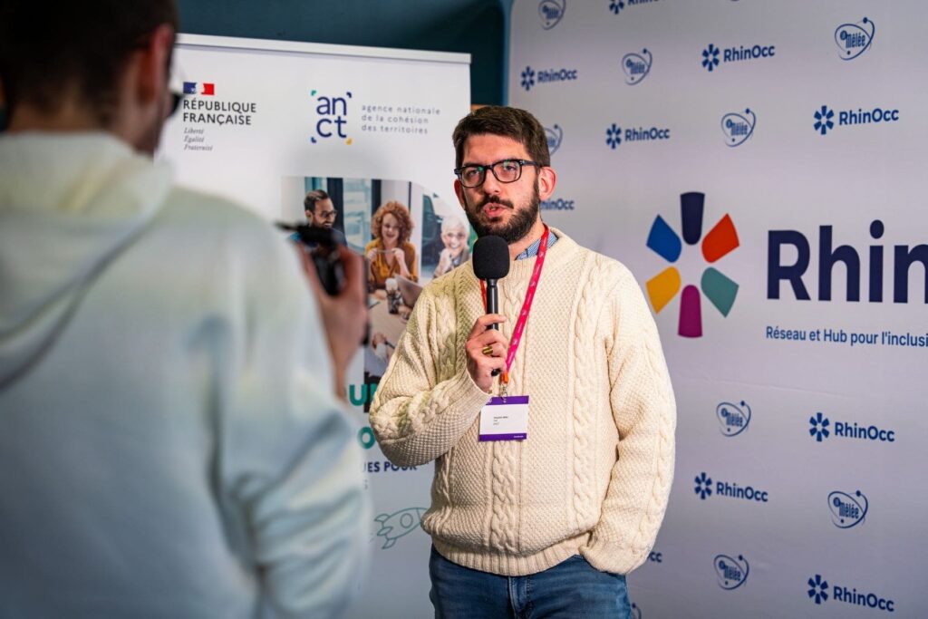Interview ANCT devant le visuel RhinOcc lors de NEC Ariège 2025 à Foix.